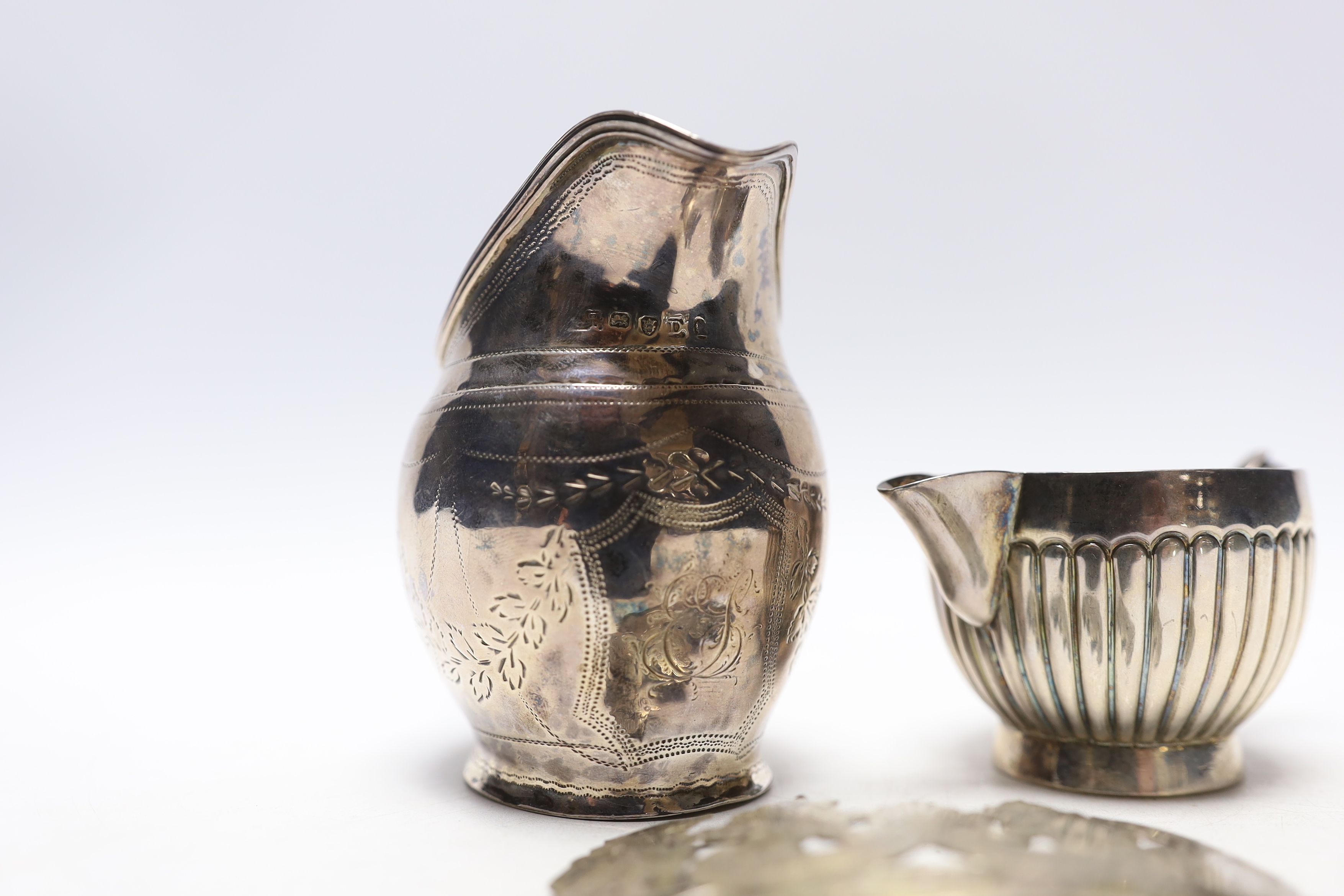 A George III silver helmet shaped cream jug, London, 1799 (a.f.), a Victorian silver cream jug by George Unite and a white metal whisky wine label.